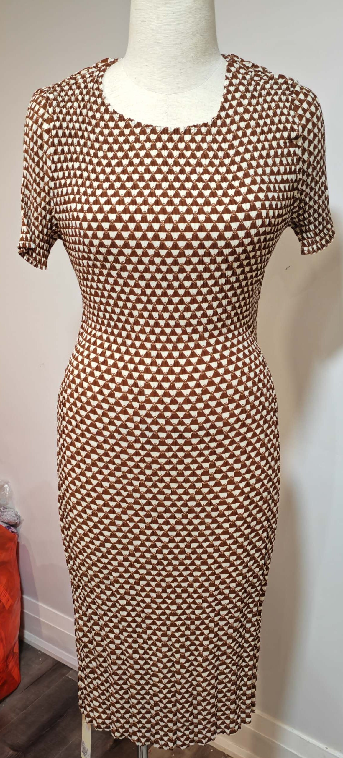 Mannequin wearing a brown geometric patterned dress against a white wall.